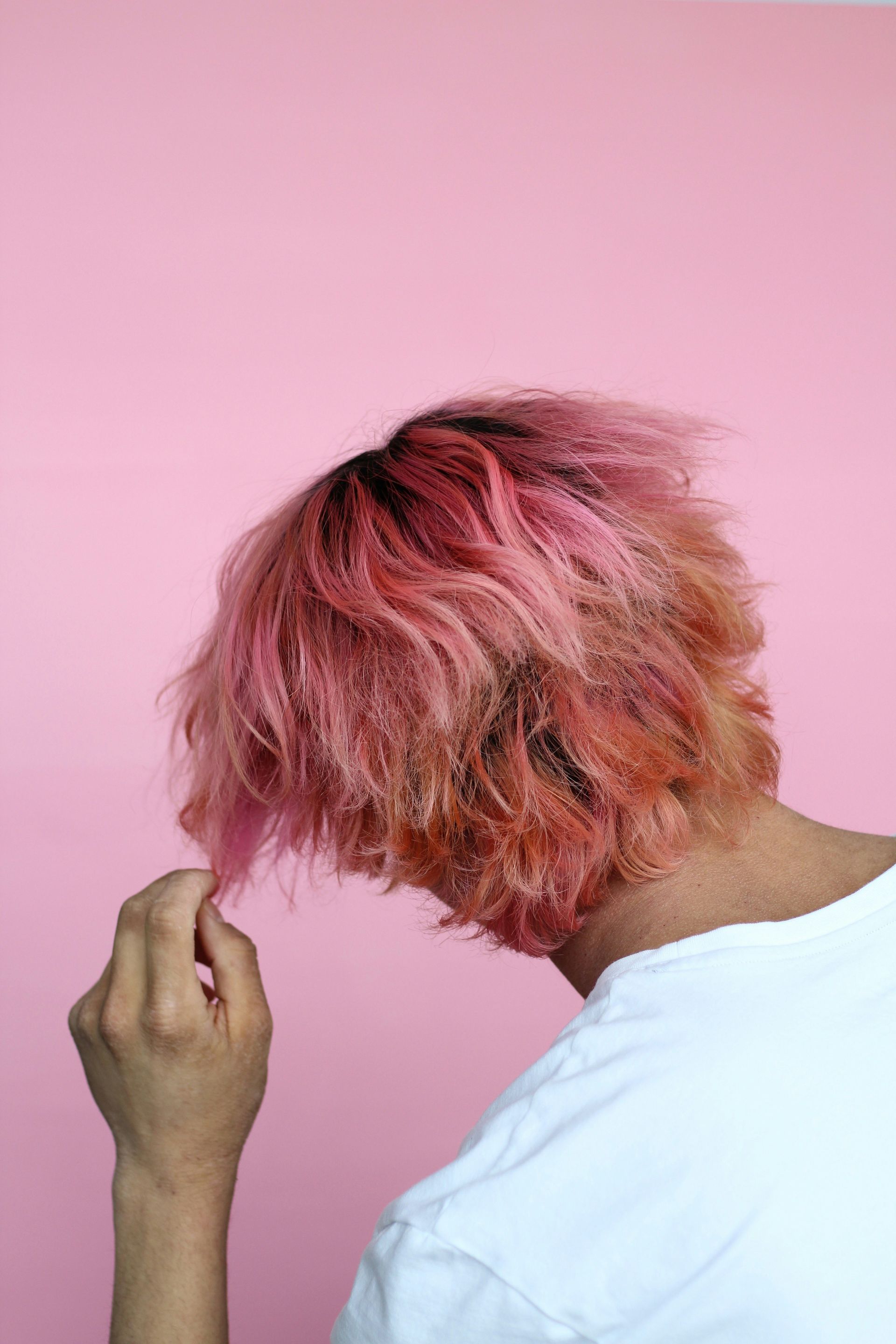 person in white top touch hair with pink dye